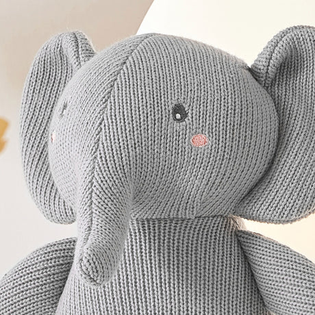 A close-up photo of a pink stuffed elephant with embroidered eyes and a stitched trunk. The elephant is made of knitted material.