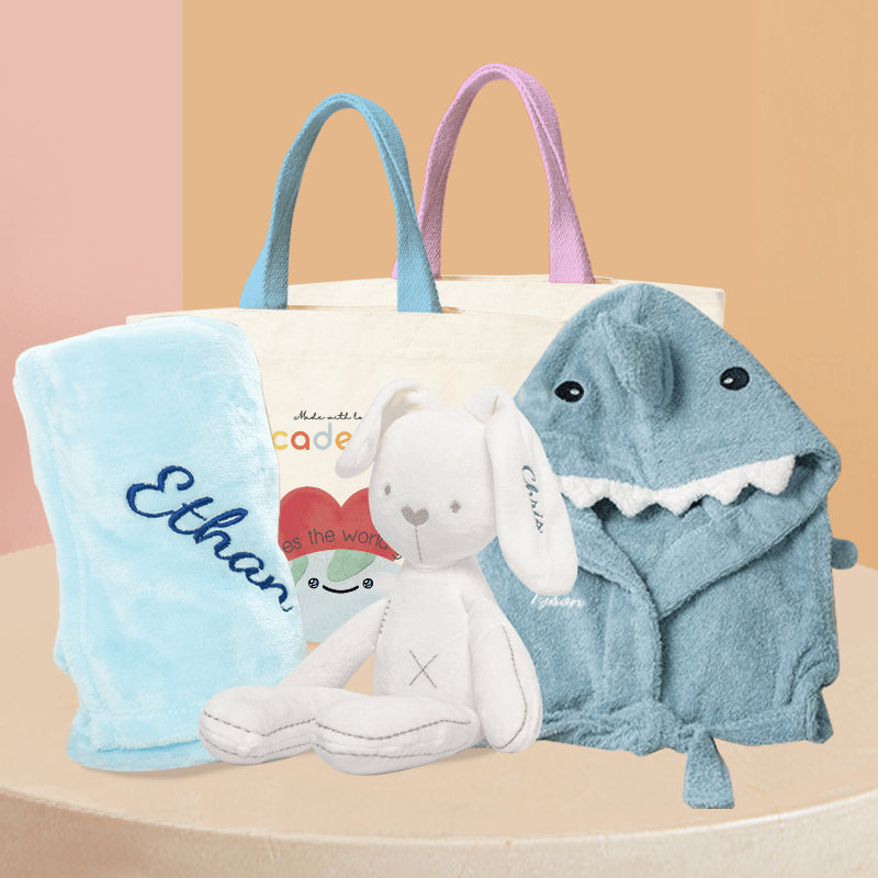 Baby Hamper - Shark Explorer Gift Set: Blue shark bathrobe, white bunny plushie, blue fleece blanket with embroidered name, and Cadeaus brand canvas bag packaging