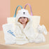 A newborn baby wearing a white bear hooded bath towel, surrounded by white soft toys and a white fleece blanket. The fleece blanket and soft toys feature embroidered names. Displaying a delightful newborn baby hamper.