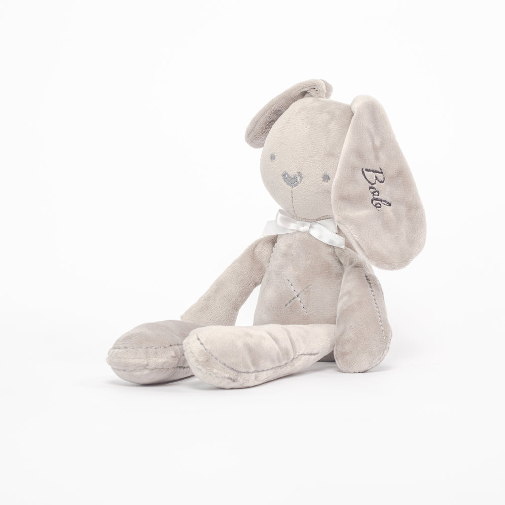 A grey bunny soft toy sitting in front of a white background, with the name &