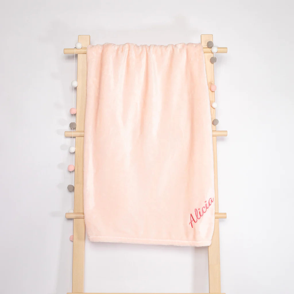 A pink fleece blanket hanging on the rack, beautifully embroidered with the name &