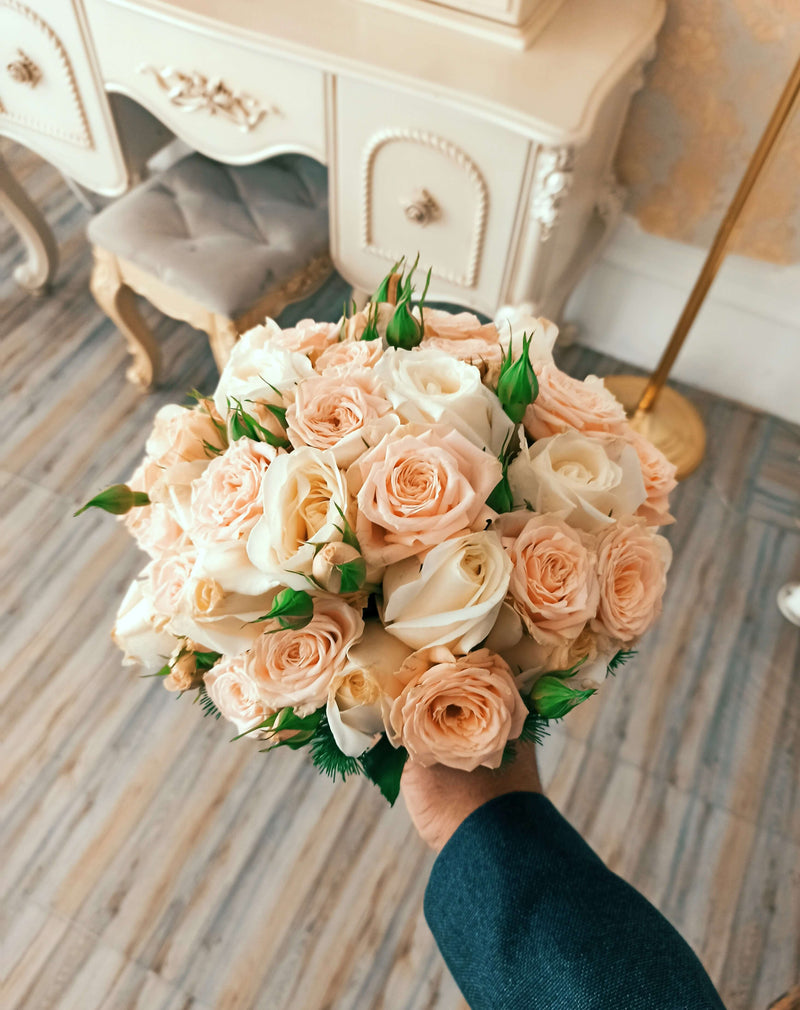Bouquet of peach and white roses held in a hand with a decorative desk in the background