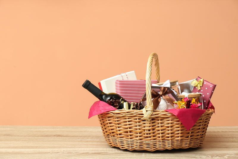 Wicker gift basket with items on a wooden surface against a peach background