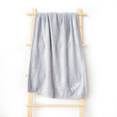 A grey fleece blanket hanging on a shelf, beautifully embroidered with the name &