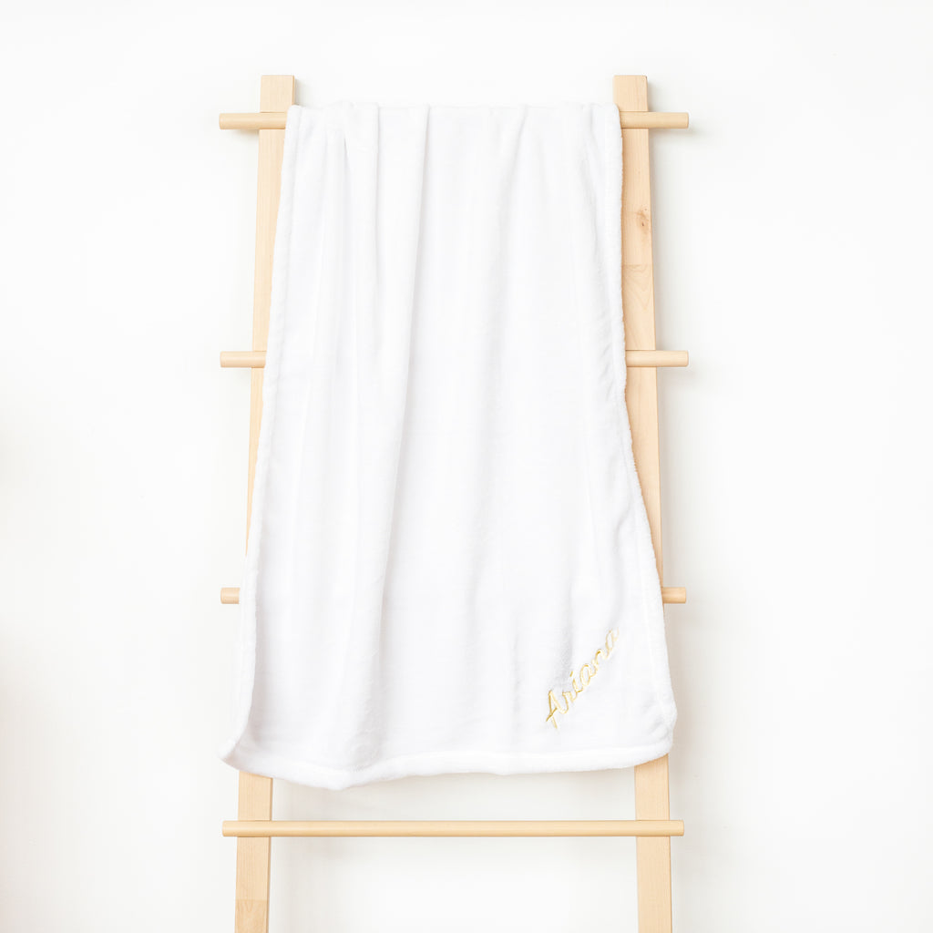 A white fleece blanket hanging on the rack, beautifully embroidered with the name &