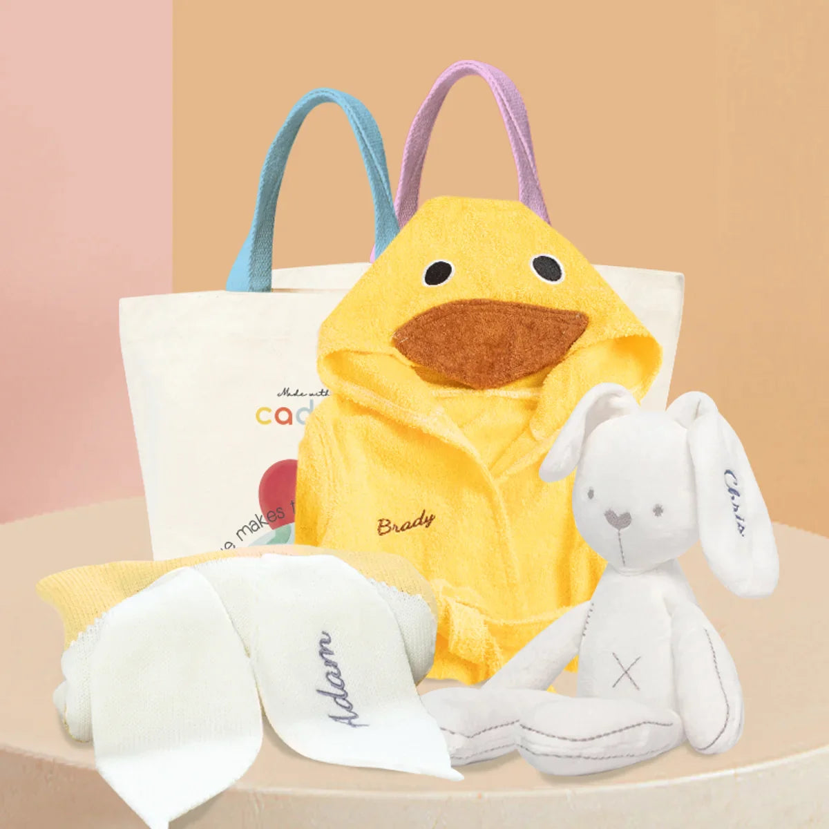 Baby Hamper - Duck Adventure Gift Set: Yellow Duck bathrobe, White bunny plushie, yellow knit blanket with embroidered name on one ear, and Cadeaus brand canvas bag packaging.