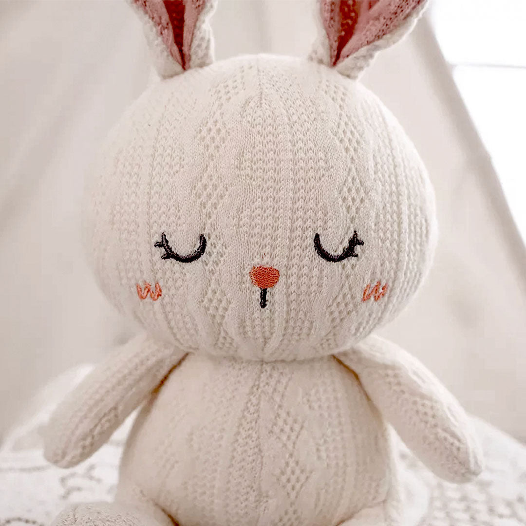 A white stuffed rabbit with its eyes closed and a pink nose.