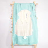 A knitted baby blanket with a bunny design on it hanging on a wooden ladder. There is text on the blanket that says "Adam".