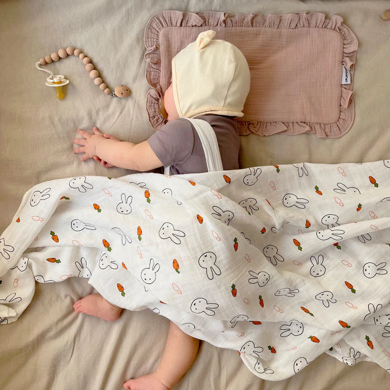 Baby sleeping under a bamboo swaddle with Miffy bunny and carrot pattern.