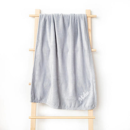 Personalized grey fleece blanket hanging on a wooden ladder, with “Mike” embroidered on the corner, highlighting its soft and plush texture.