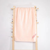 Personalized pink fleece blanket with the name Alicia, hanging on a wooden ladder, showcasing its soft and cozy texture.