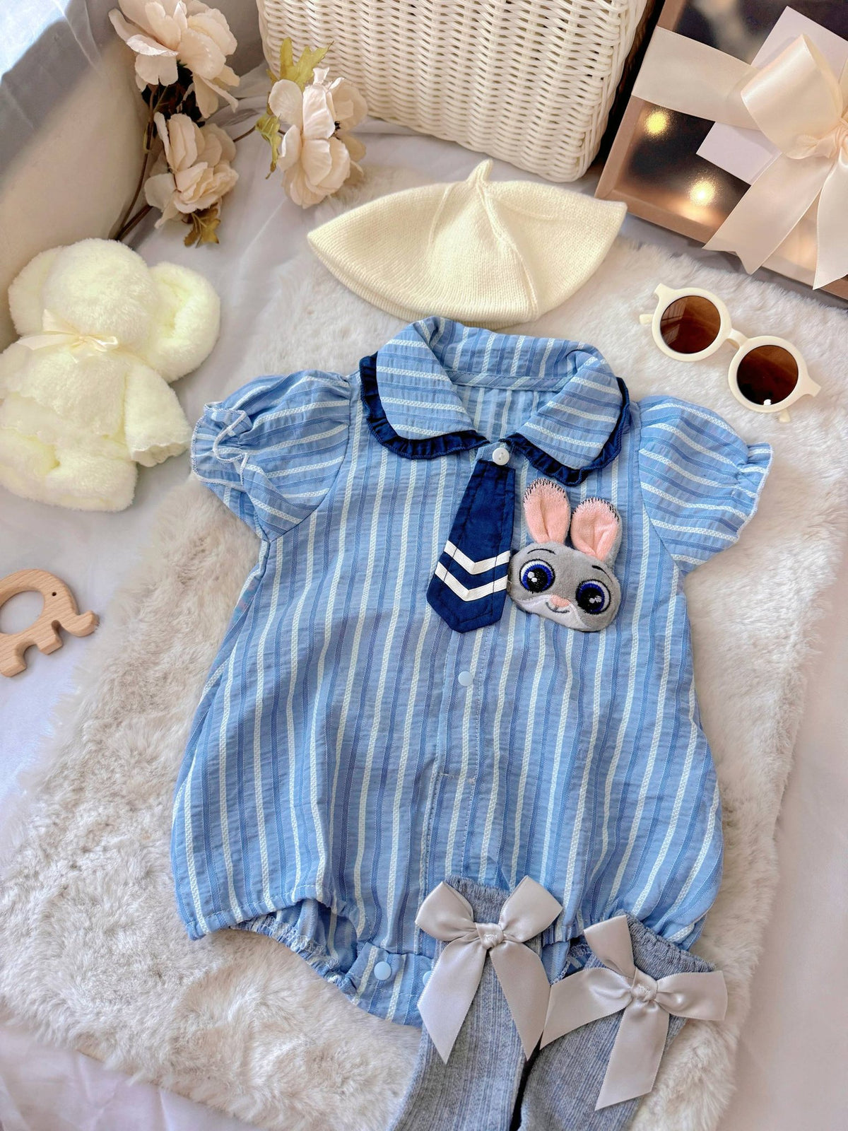 Judy Bunny baby outfit flat lay – blue striped romper with tie and bunny badge