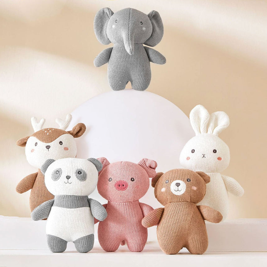 A group of stuffed animals are crowded together on a wooden shelf. The stuffed animals include a rabbit, a bear, a deer, an elephant, and a pig. They are all different colors and sizes.