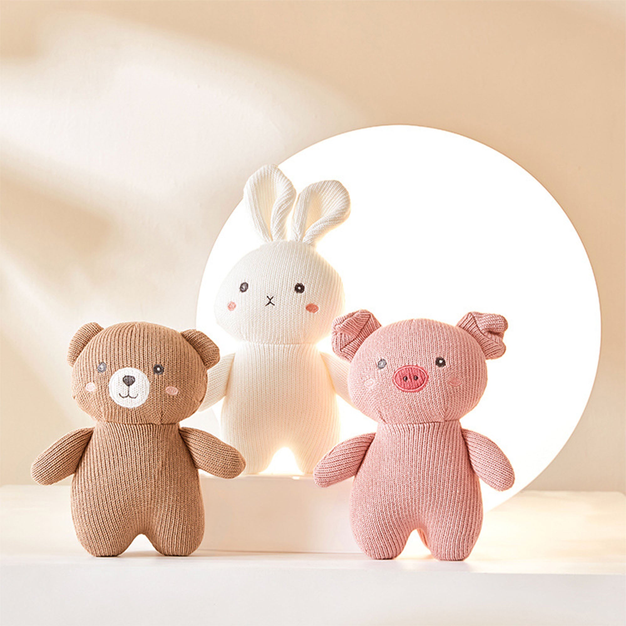 Three stuffed toys sit on a shelf: a brown teddy bear, a white bunny, and a pink pig.