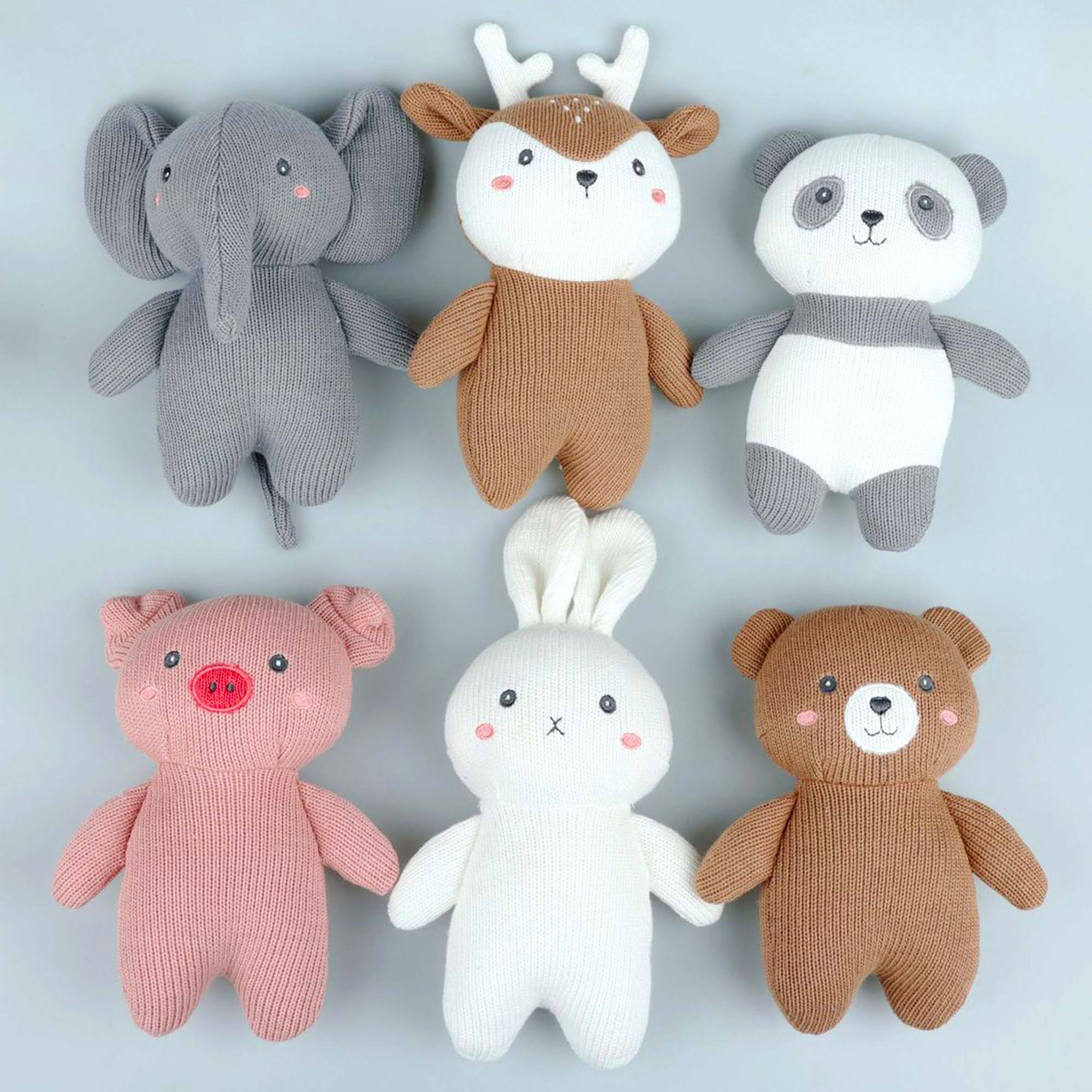 A group of knitted stuffed animals sit next to each other on a wooden table. The stuffed animals include a elephant, reindeer, panda, piggy, bunny and a bear. They are all made from colorful yarn.