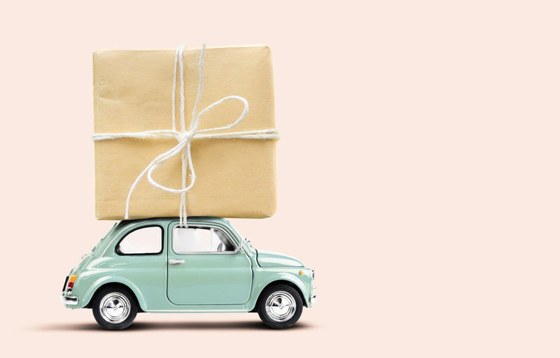 Toy car carrying a wrapped gift on a beige background