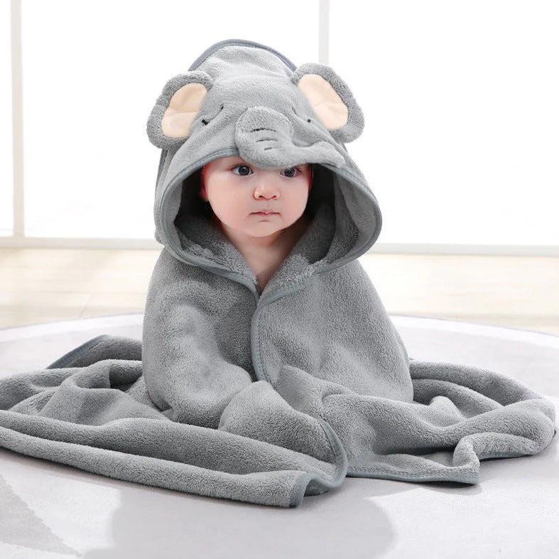 Baby sitting on the floor wearing a grey elephant hooded bath towel, with floppy ears and an embroidered elephant face, looking cute and comfortable.