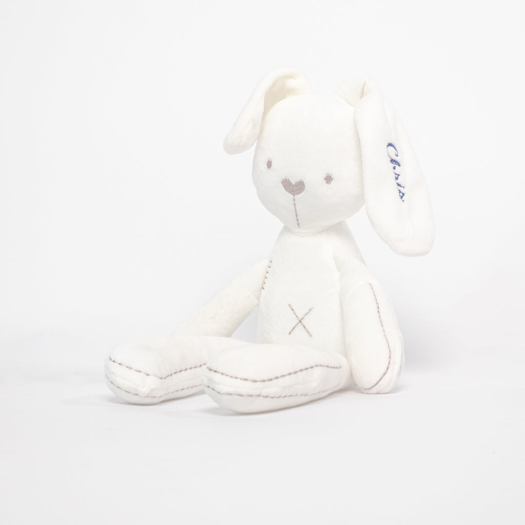 A white bunny soft toy sitting in front of a white background, embroidered with the name Chris.