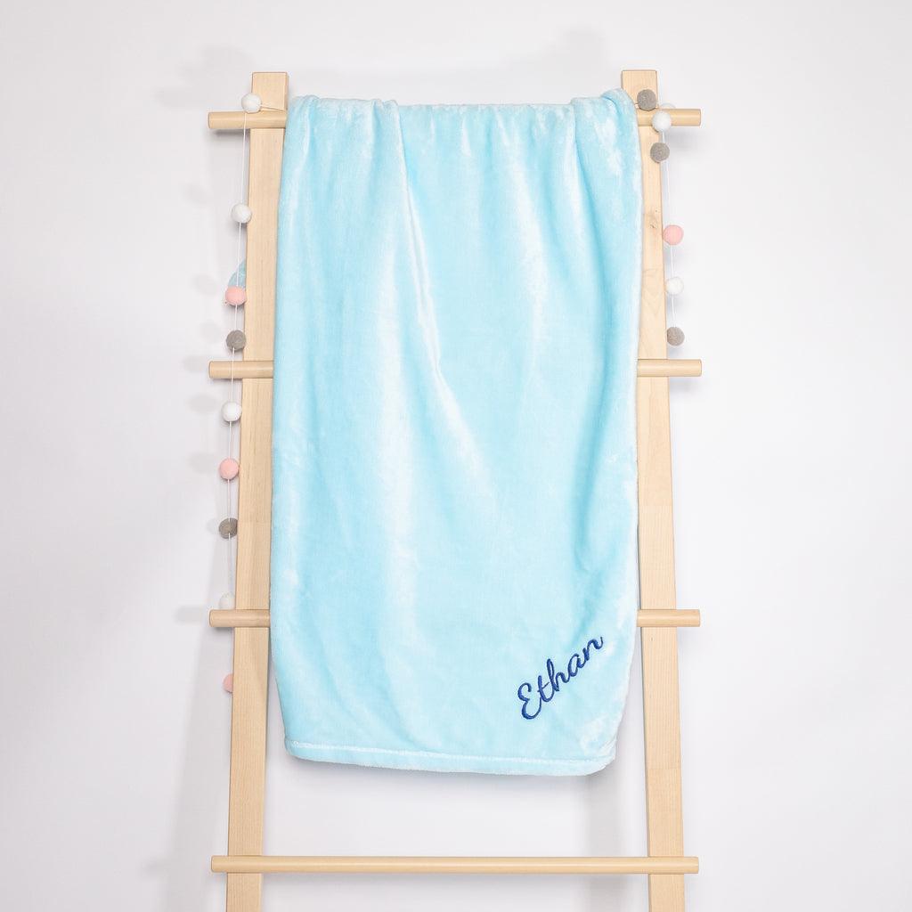 Light Blue Fleece Blanket with the name embroidered hanging on the wooden rack.