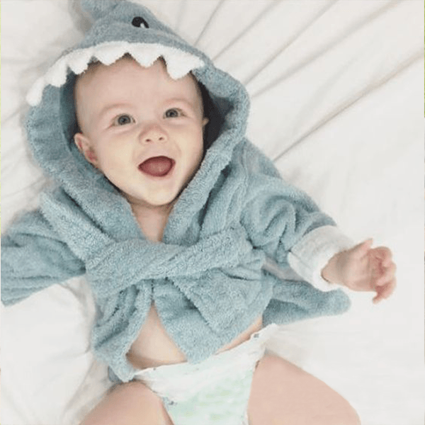 Baby wearing a Blue Shark bathrobe laying on the bed.
