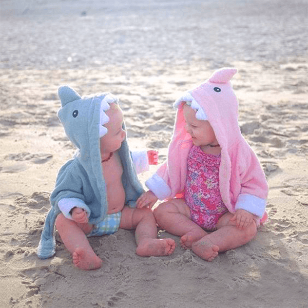 two babies wearing pink and blue shark bathrobe on a beach