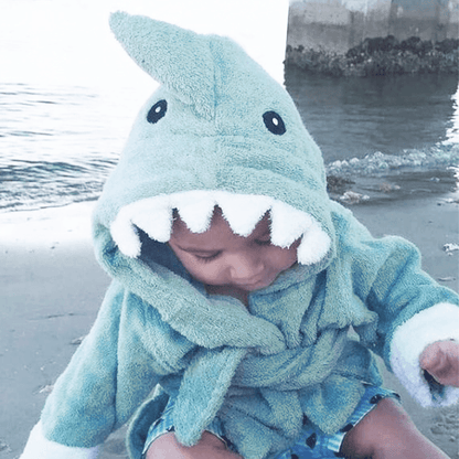 a baby wearing a shark bathrobe playing at the beach