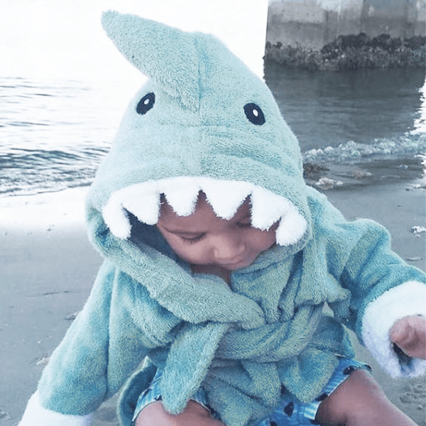 a baby wearing a shark bathrobe playing at the beach