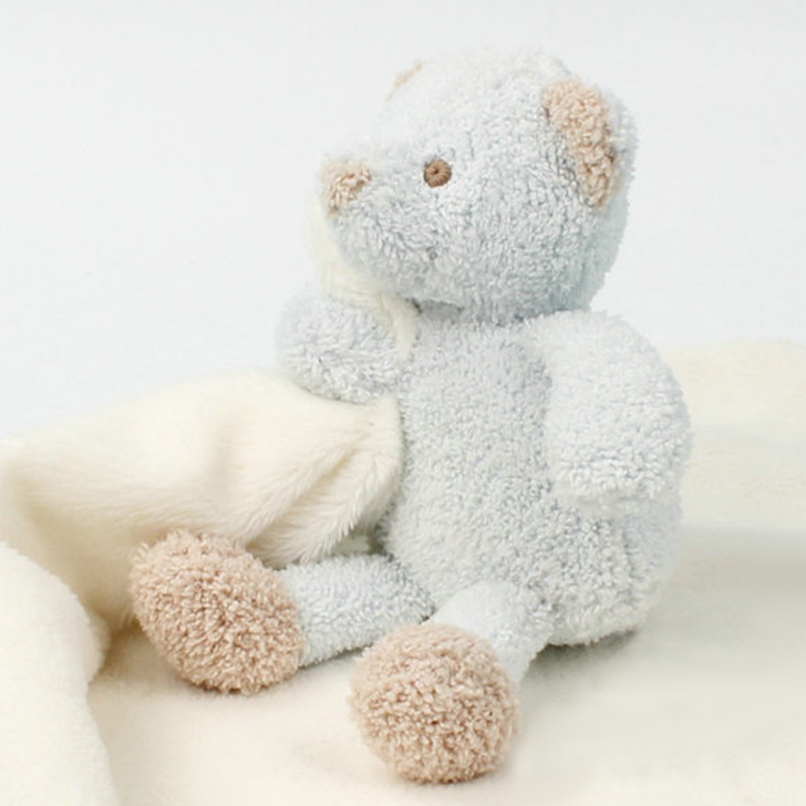 a stuffed animal - blue bear sitting on top of a white blanket.