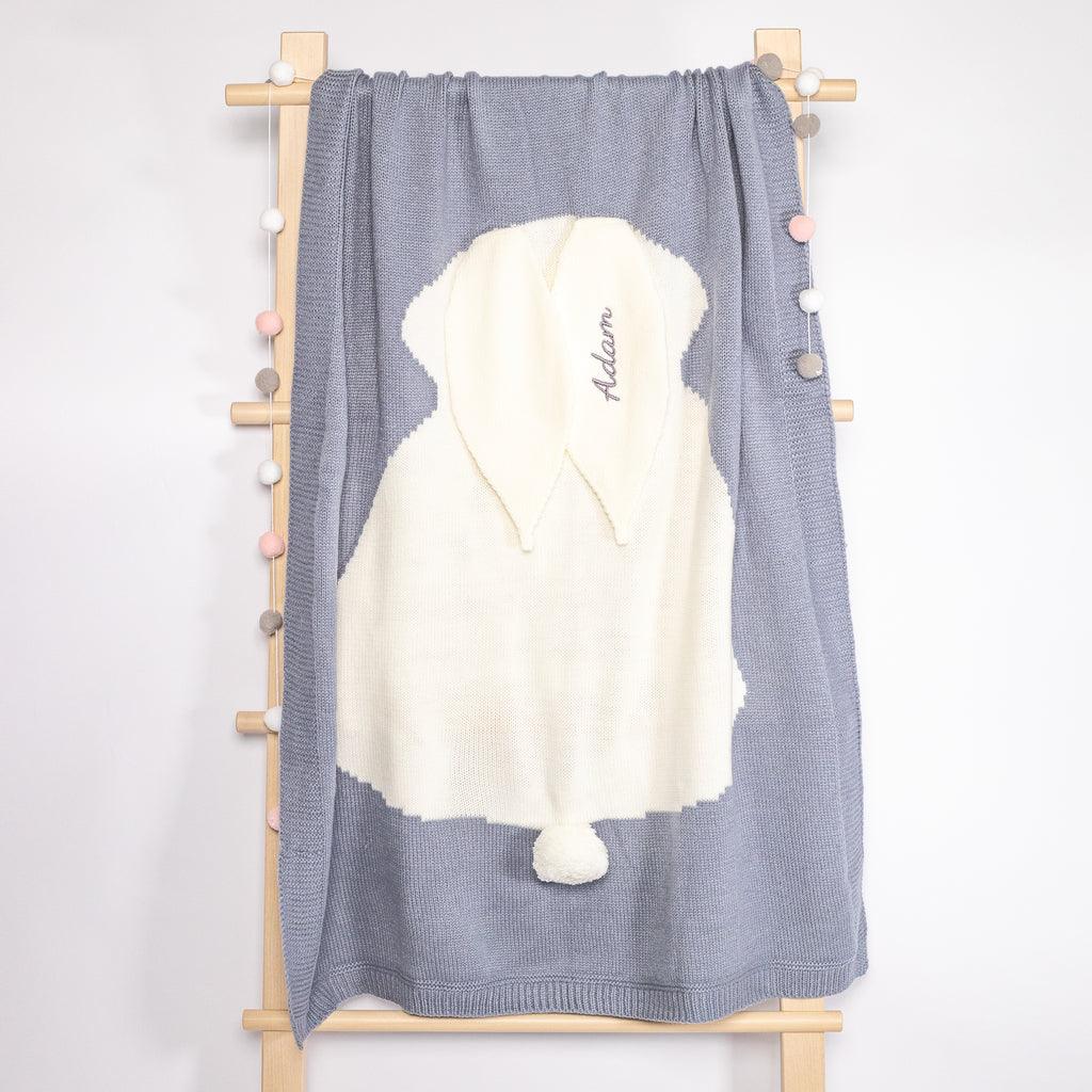 A grey knit blanket hanging on the rack, beautifully embroidered with the name &