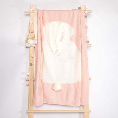 A pink bunny knit blanket hanging on the rack, beautifully embroidered with the name &